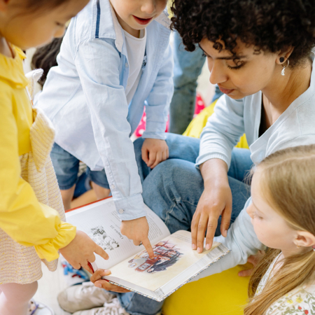 Des enfants regardent un livre en anglais avec leur animatrice