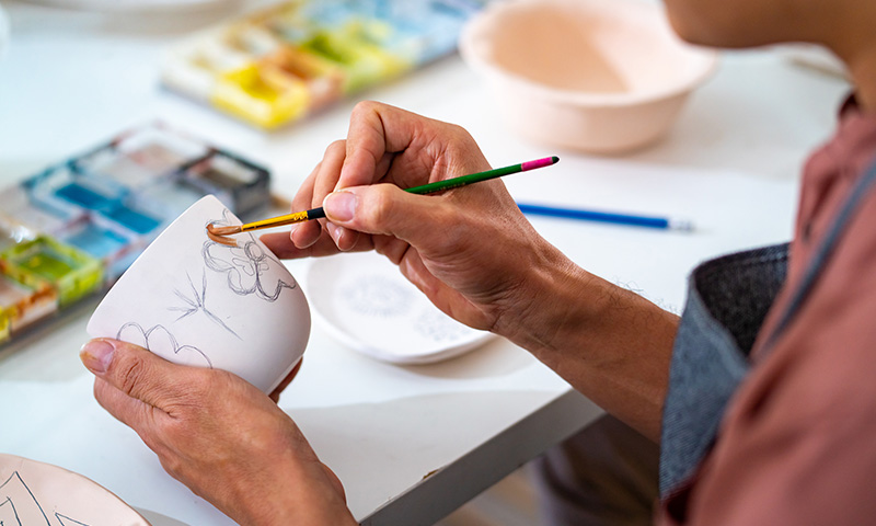 Un homme peint une tasse dans un atelier de peinture sur porcelaine