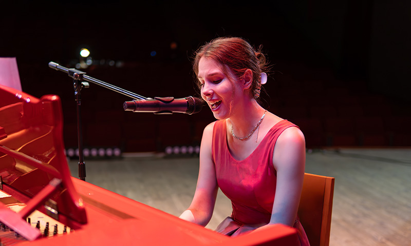 Femme jouant du piano en chantant sur scène lors d'un concert, illustration de l'atelier piano voix